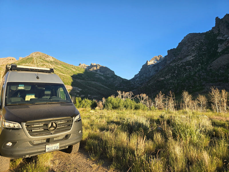 Mercedes-Benz Sprinter RV rental amidst sunlit mountains & grass. Enjoy scenic off-grid adventures & van life exploring nature. — photo 8