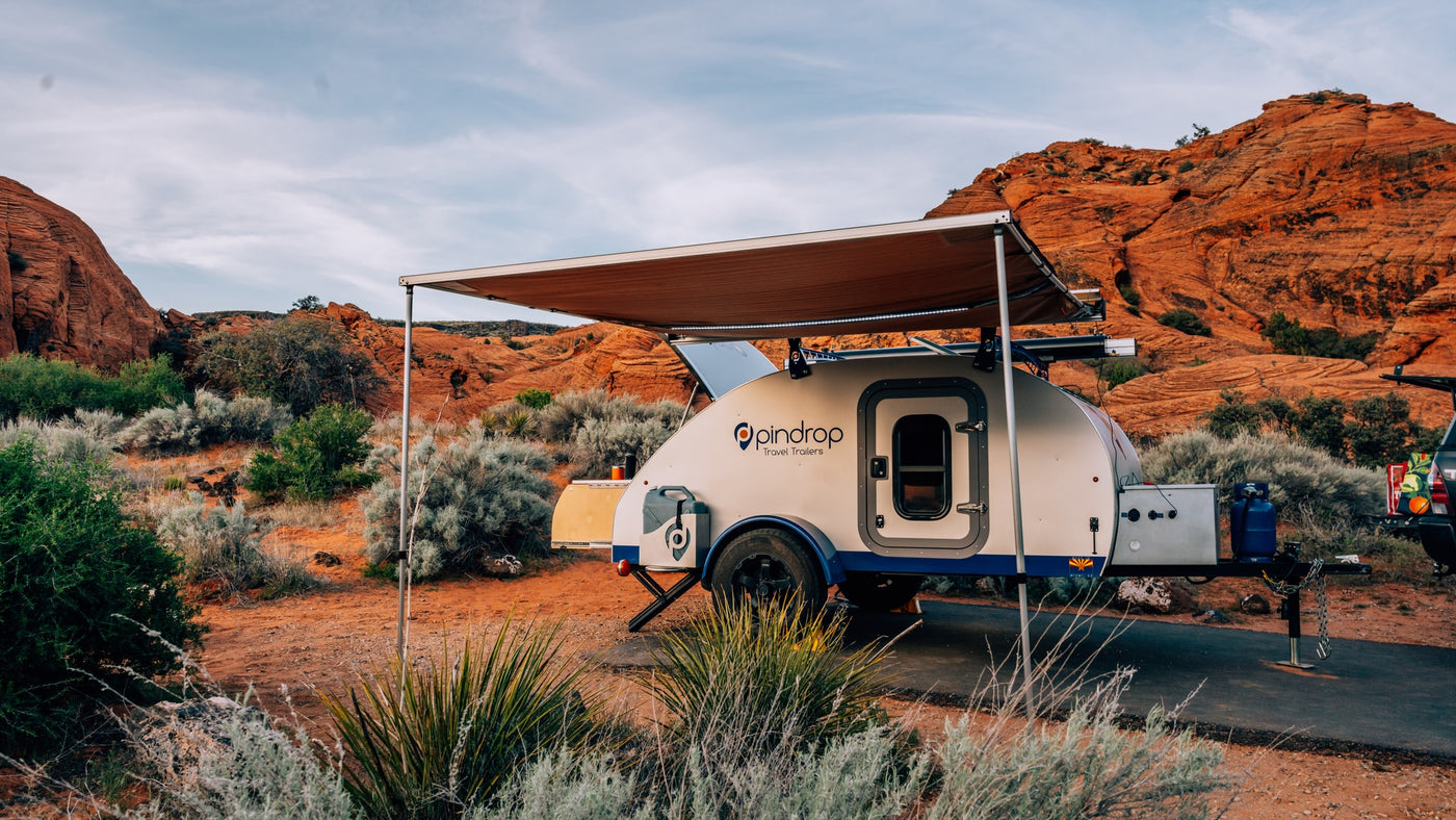 This Pindrop teardrop RV rental, with its side awning extended, is parked in a vibrant desert landscape with red rock formations. — photo 8
