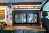 This RV rental shows a cozy kitchen with a butcher block counter, sink, and forest window view. A fan, outlets, and Renogy monitor are visible.