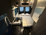 This RV rental interior reveals a compact kitchen (sink, stovetop), a versatile bed, and integrated storage solutions.