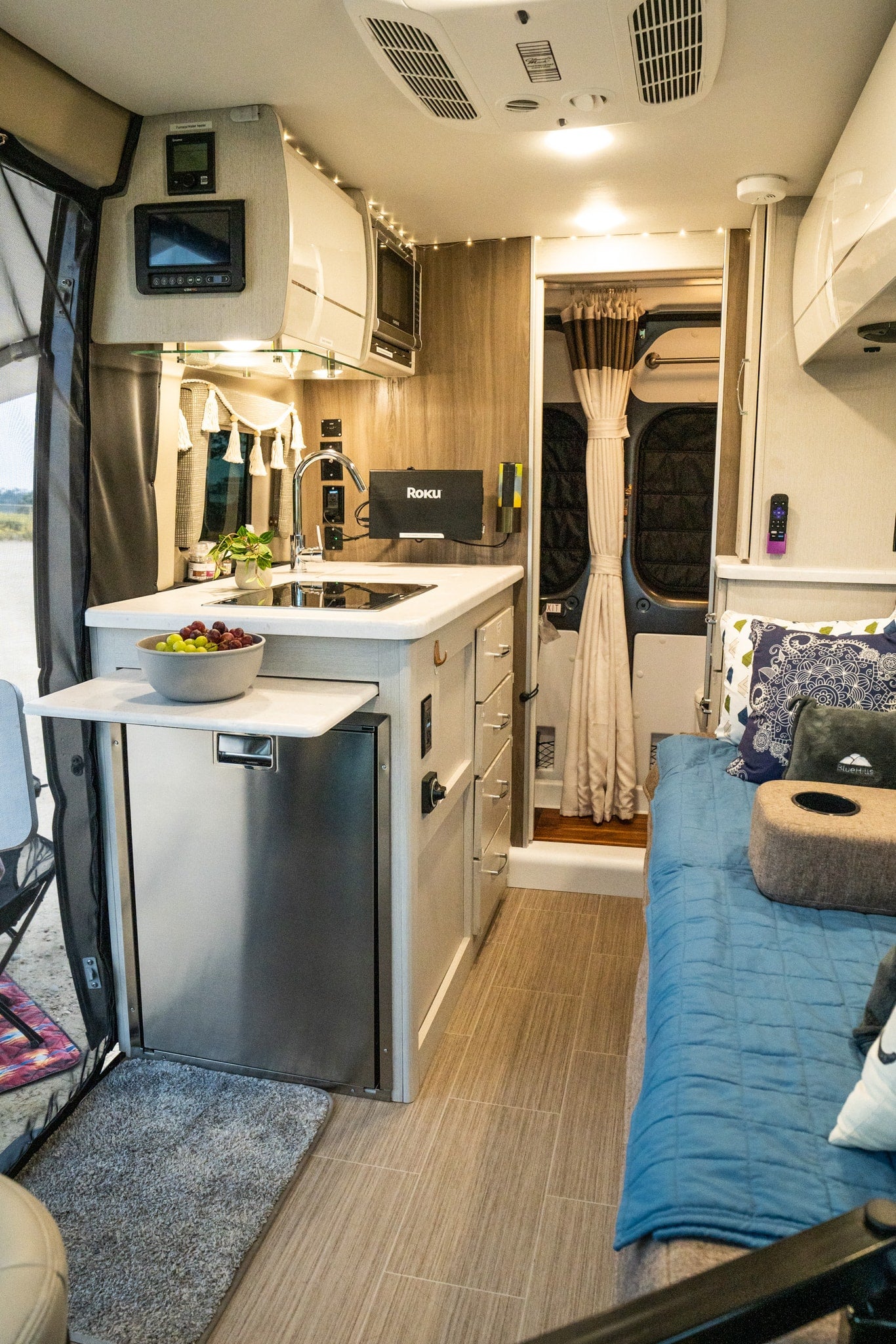 RV rental's bright interior: compact kitchen (sink, microwave, fridge), bed, and controls for a comfortable journey. — photo 7