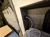 RV rental charging nook: Fabric-lined cubby with illuminated USB port & white cable. Bed, table & pleated window shade for comfort.
