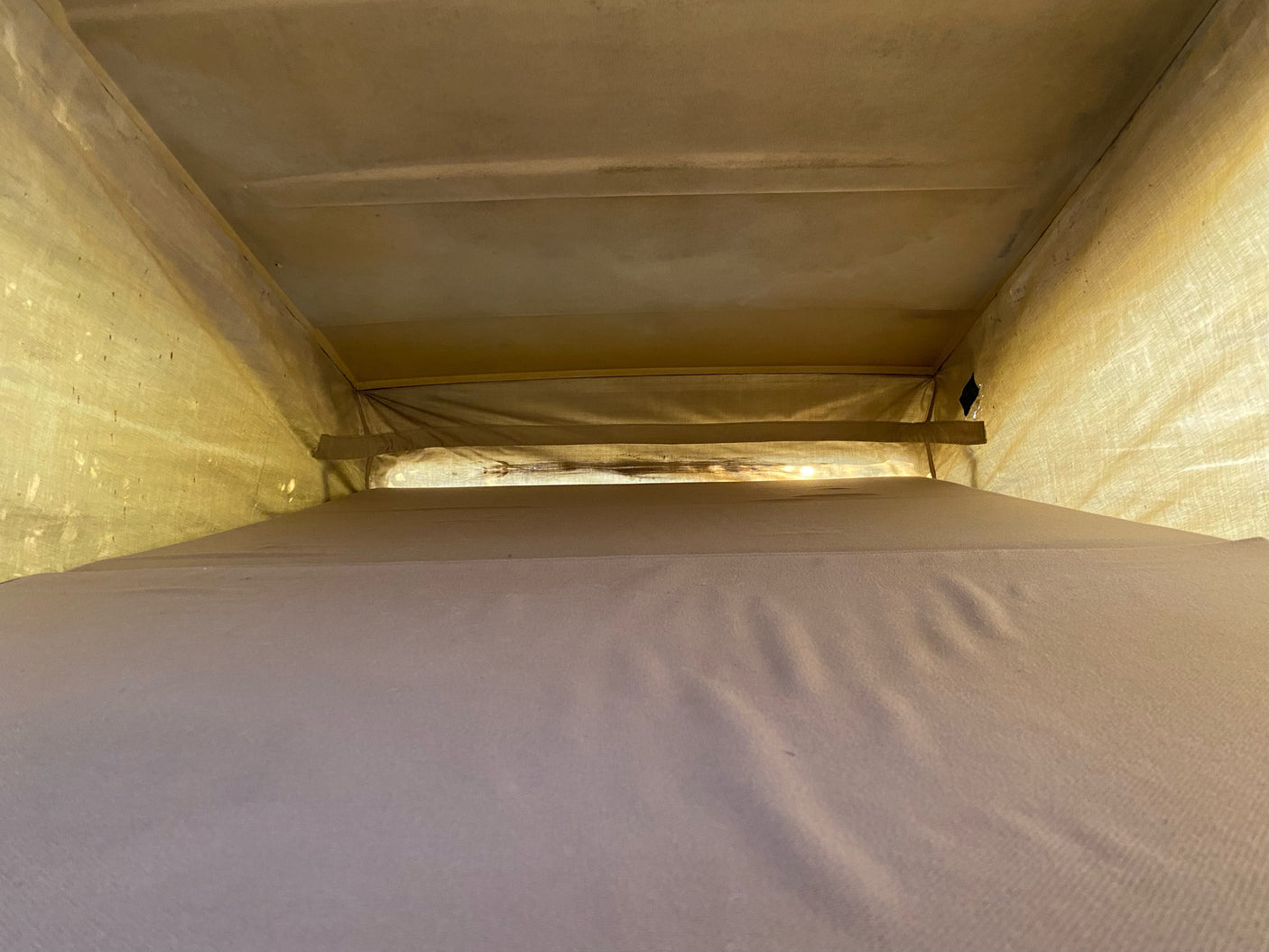 Inside an RV rental pop-top, showing the cozy upper sleeping area with light filtering through the fabric walls and ceiling.