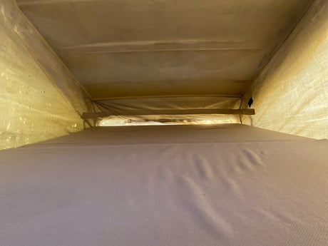 Inside an RV rental pop-top, showing the cozy upper sleeping area with light filtering through the fabric walls and ceiling.