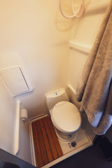 This RV rental's compact wet bath features a white toilet, shower hose, drain, and a practical wooden slatted mat.