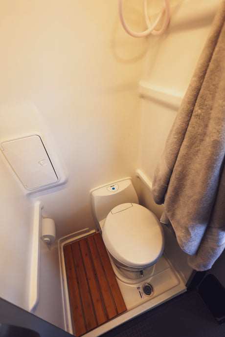 This RV rental's compact wet bath features a white toilet, shower hose, drain, and a practical wooden slatted mat.