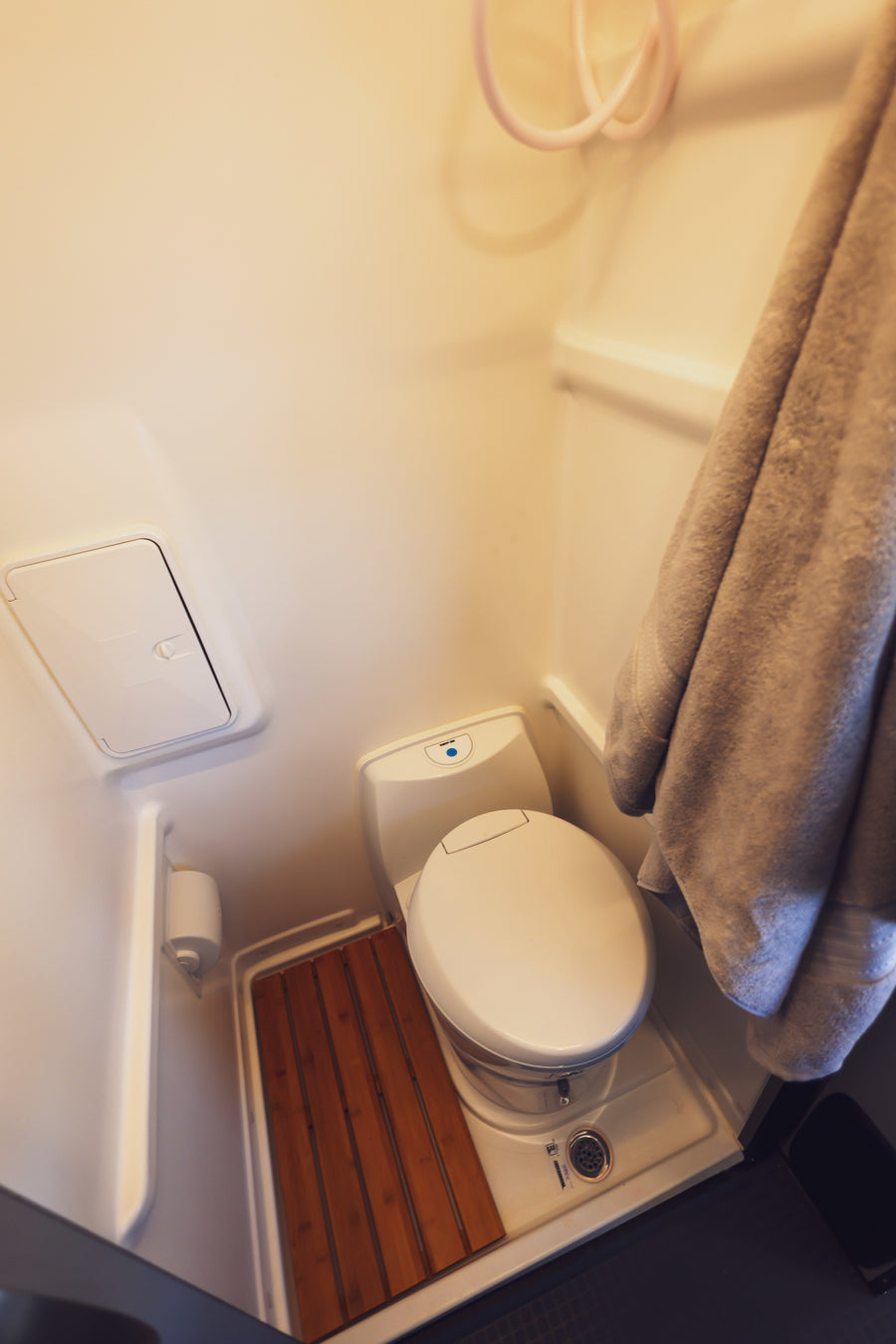 This RV rental's compact wet bath features a white toilet, shower hose, drain, and a practical wooden slatted mat.