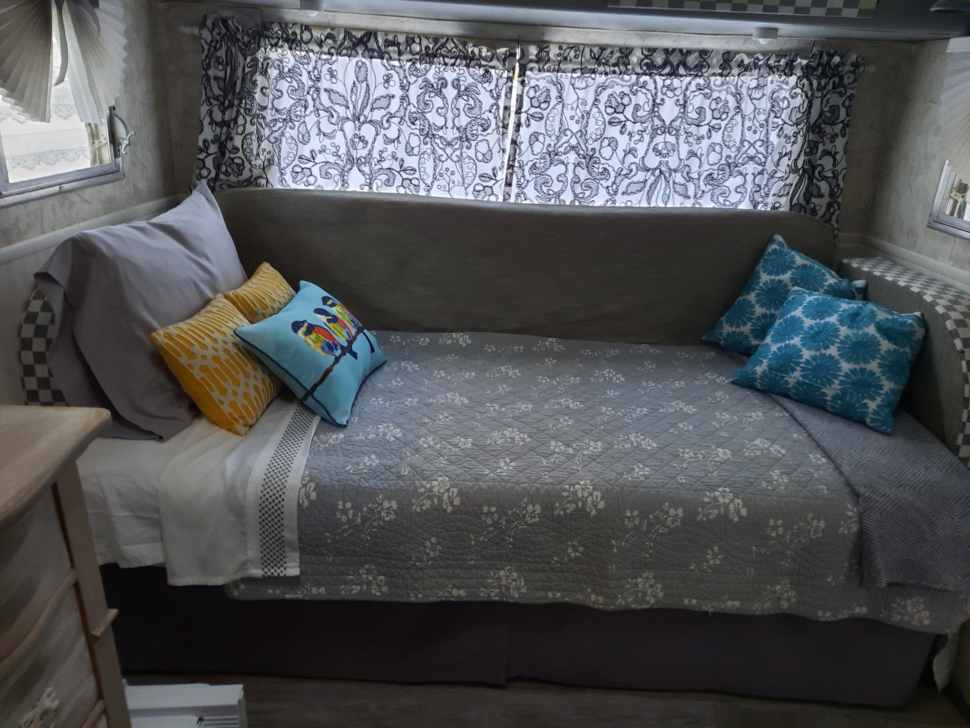 Cozy RV rental bedroom featuring a bed with a floral quilt, colorful pillows, and decorative patterned curtains. — photo 5