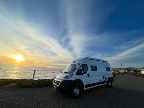 White Winnebago Solis RV rental parked oceanfront at a fiery sunset, perfect for coast adventures.