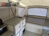 Inside this RV rental, a pop-up camper features a kitchenette with sink, storage, and a spacious bed.