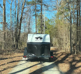 Rear view of a Rustic Trail camping trailer on a wooded path, perfect for an RV rental outdoor adventure.