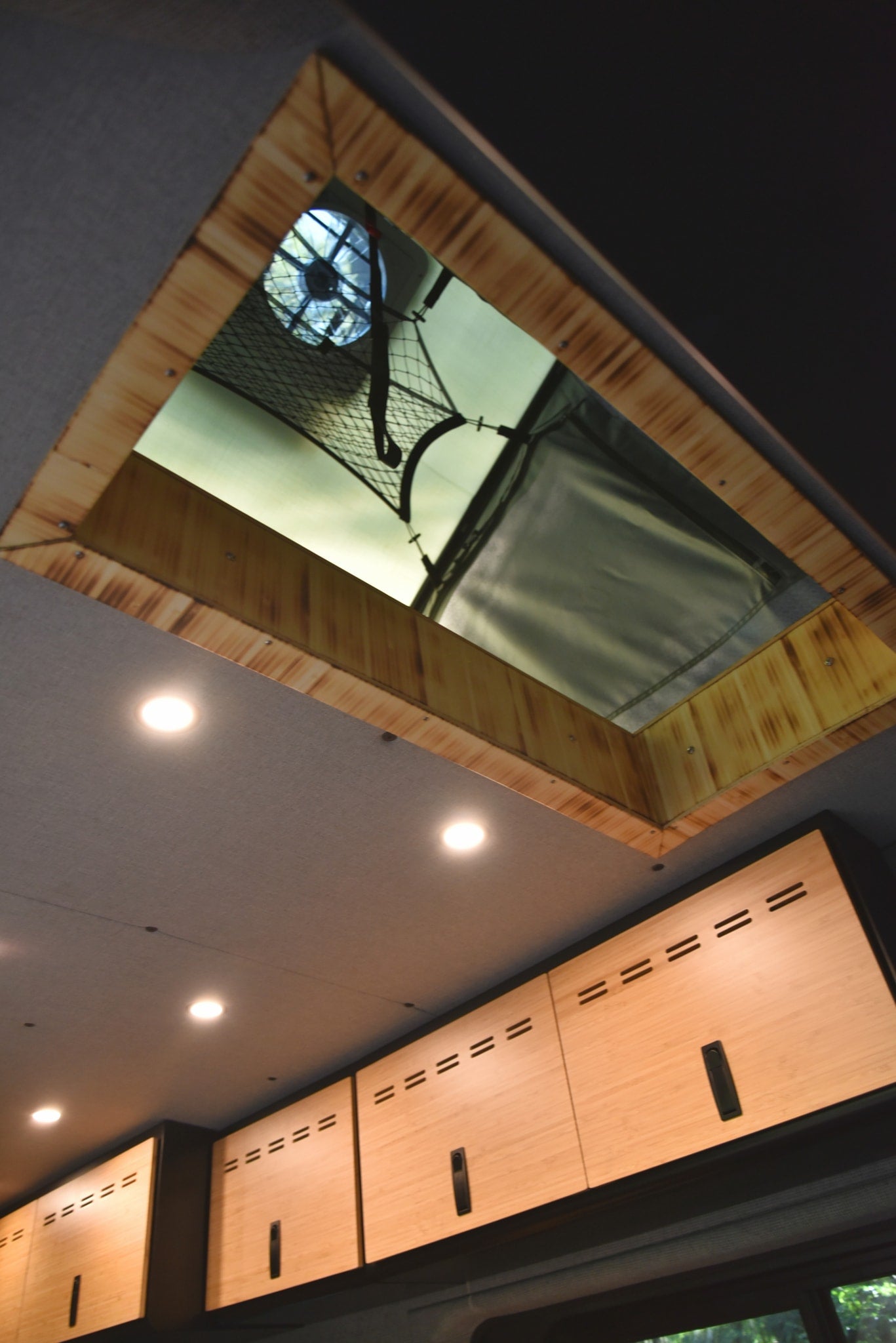 Bright RV rental interior with a ceiling vent, LED lighting, wooden cabinets, and an overhead cargo net for storage. — photo 10