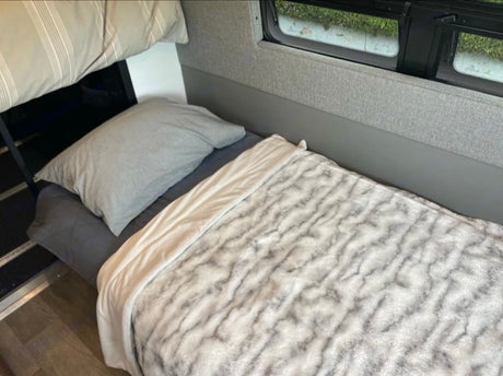 Cozy RV rental bunk bed with soft grey bedding & patterned blanket, next to a window.