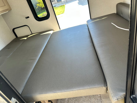 Spacious RV rental interior with a gray convertible bed and bright window view, ready for your camper trip.