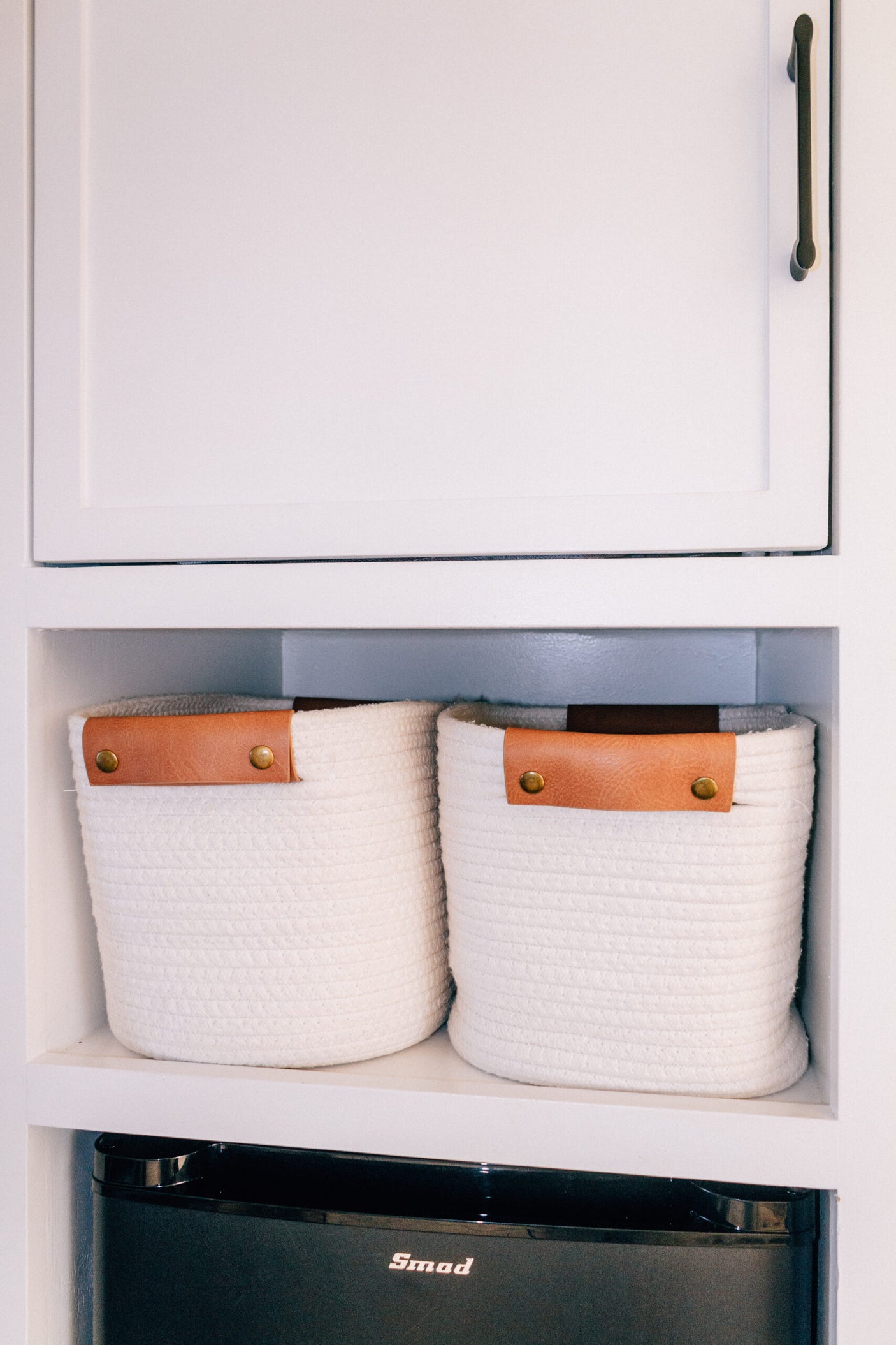 RV rental interior featuring neat storage: two white rope baskets on a shelf above a black Smod mini-fridge.