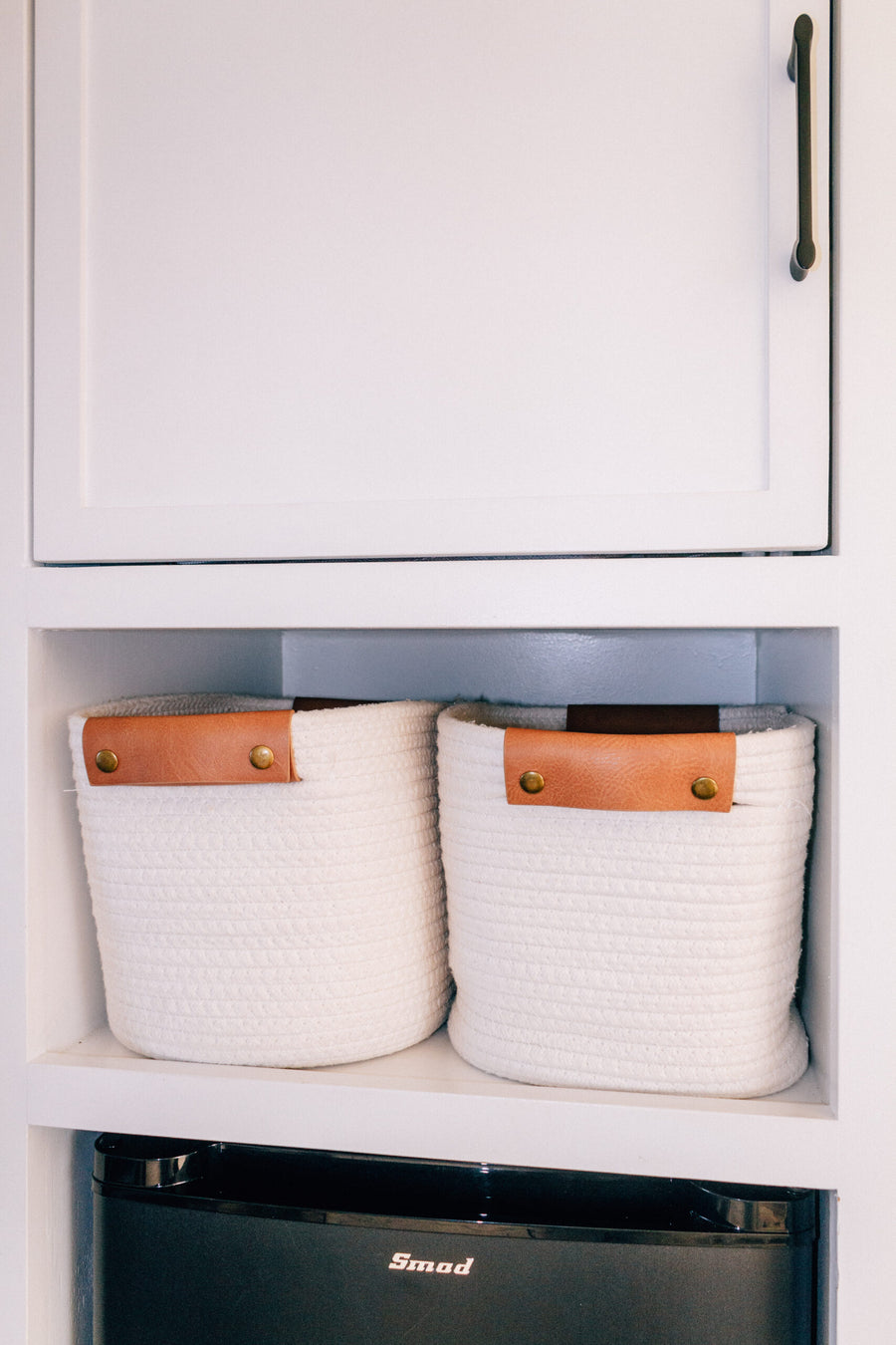 RV rental interior featuring neat storage: two white rope baskets on a shelf above a black Smod mini-fridge.