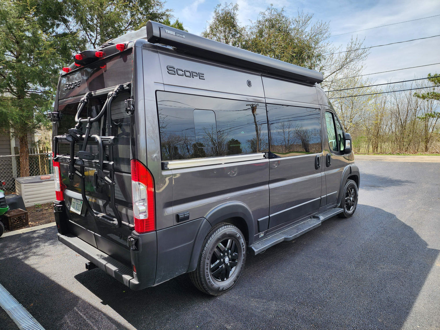 Modern gray RV rental parked on asphalt, featuring a Thule awning and bike rack, ready for your next trip.