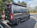 Modern gray RV rental parked on asphalt, featuring a Thule awning and bike rack, ready for your next trip.