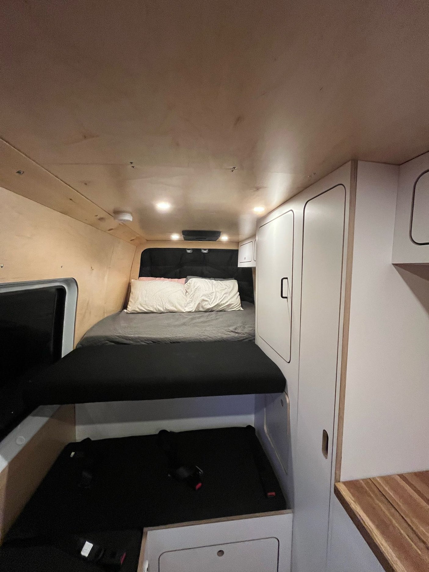 Cozy RV rental interior featuring a bed, wood paneling, white cabinets, and convenient under-bed storage.