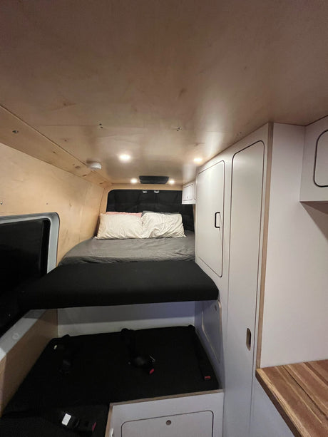Cozy RV rental interior featuring a bed, wood paneling, white cabinets, and convenient under-bed storage.