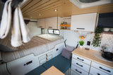 Cozy RV rental interior featuring a comfortable bed, modern kitchen with hex tiles, wood ceiling, and smart storage.