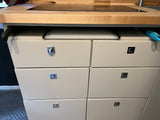 RV rental kitchen space: light wood counter with induction hob, pull-out cutting board, and compact storage drawers.