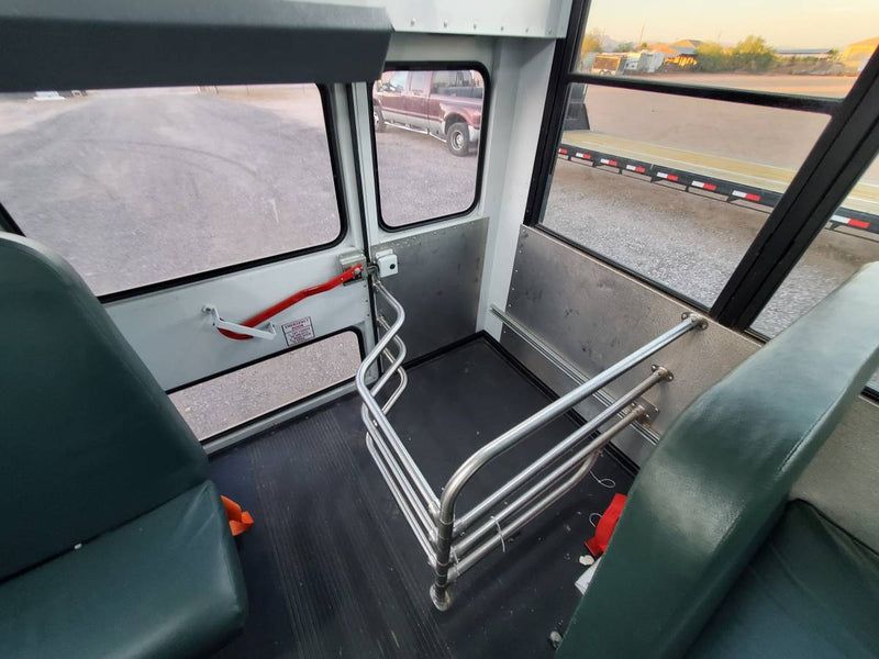 Inside an RV rental, showing green seats, a red emergency exit, and a metal safety railing. Gravel lot visible outside. — photo 3