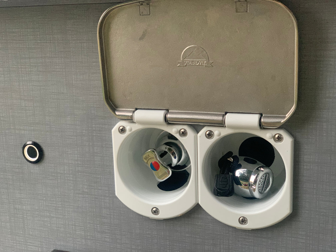 RV rental outdoor shower with lid open, revealing a chrome mixer tap (hot/cold) and a small shower head. — photo 17