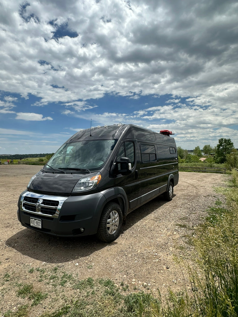 Stylish black camper van, ideal for RV rental adventures. Parked on a gravel lot under a partly cloudy sky. — photo 18