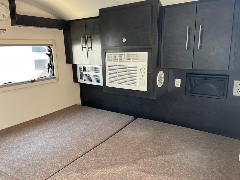 Inside an RV rental: a sleeping area with dark cabinets, a window, and two air conditioning units. — photo 3