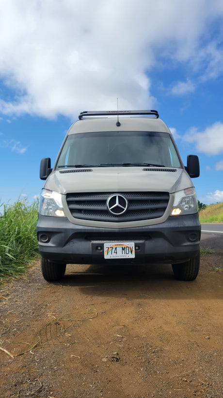 RV rental: Front view of a gray Mercedes-Benz Sprinter camper van parked on a dirt shoulder in Hawaii.