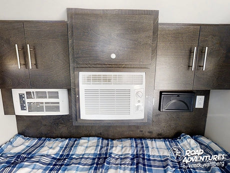 Comfort in your RV rental: a compact sleeping area with two built-in AC units, dark wood cabinets & plaid bed.