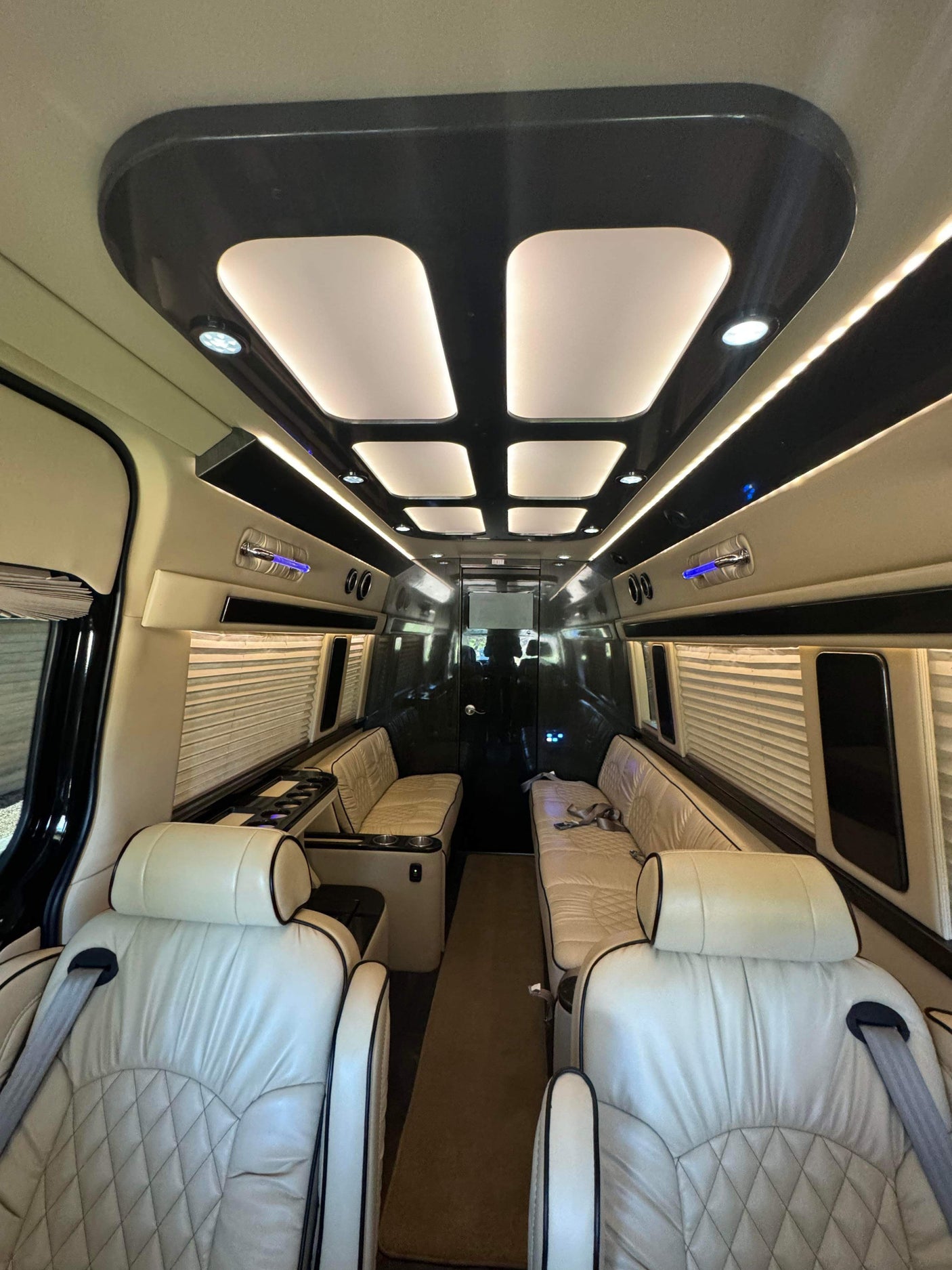 Luxury RV rental: View inside a custom van featuring cream quilted leather seats, ambient lighting, and window blinds.