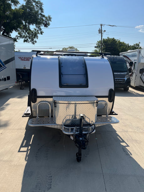 White teardrop trailer with large front window & diamond plate storage, perfect for rv rental. Sunny lot.