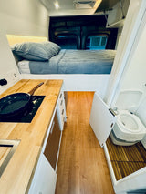 Explore this compact RV rental! Features an elevated bed, kitchenette with induction cooktop, and a cleverly hidden portable toilet.