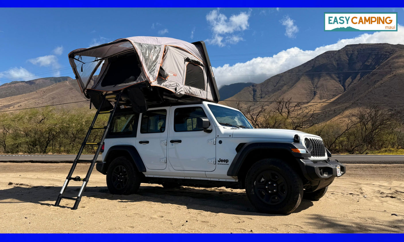 A white Jeep Wrangler with a deployed rooftop tent, parked on sand near mountains. Your next adventure RV rental for camping is ready!