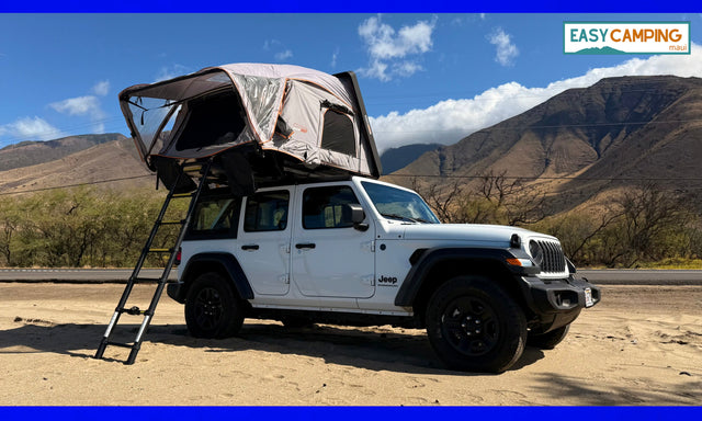 A white Jeep Wrangler with a deployed rooftop tent, parked on sand near mountains. Your next adventure RV rental for camping is ready!