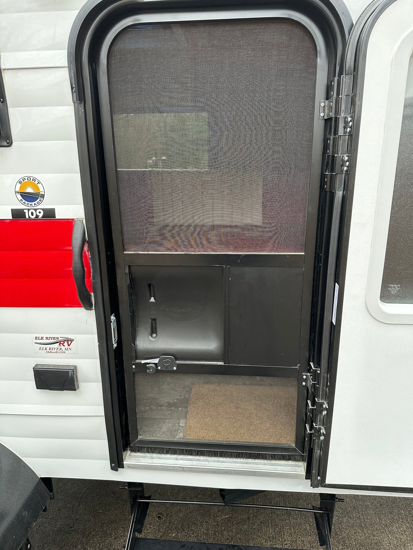Exterior view of an RV rental's open screen door, showing entry steps, interior mat, and side panel. — photo 9