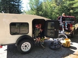 Kids relaxing at their rv rental campsite, ready for adventure with bikes & gear, next to a red pickup truck.