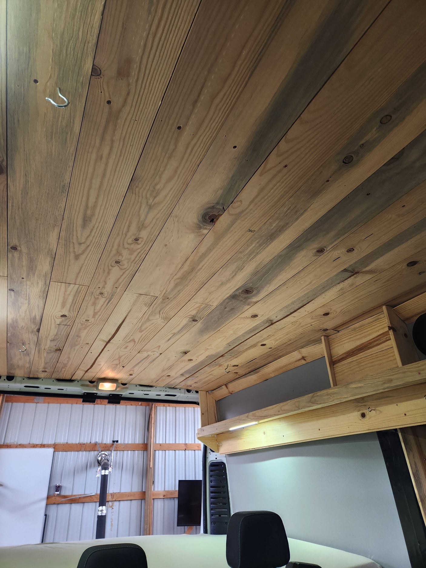 RV rental interior: bespoke wood ceiling with hook & light, featuring wooden storage & LED lighting. Shows vehicle rear.
