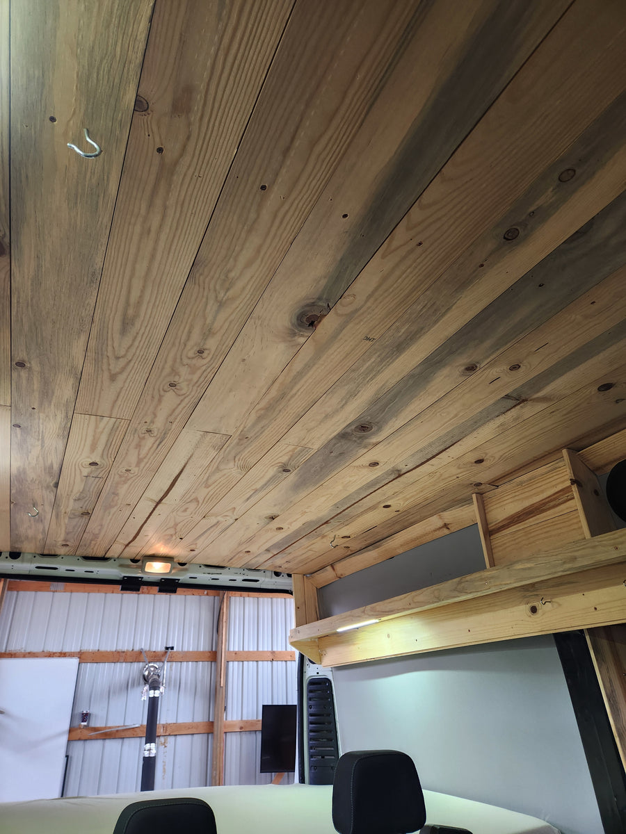 RV rental interior: bespoke wood ceiling with hook & light, featuring wooden storage & LED lighting. Shows vehicle rear.