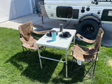 Outdoor dining by a small RV rental: two camo chairs, a table with dishes & cups. Ideal for your next camp adventure!