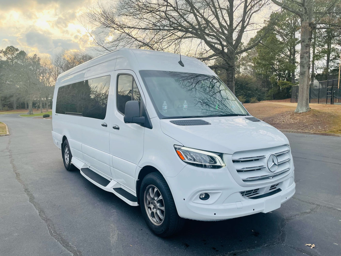 Spotless white Mercedes-Benz Sprinter van, ideal for RV rental. Parked on asphalt with trees in the background.
