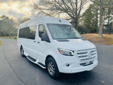 Spotless white Mercedes-Benz Sprinter van, ideal for RV rental. Parked on asphalt with trees in the background.