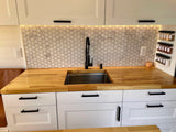 RV rental: Modern kitchen with white hex tile backsplash, butcher block countertops, black faucet, and under-cabinet lighting.