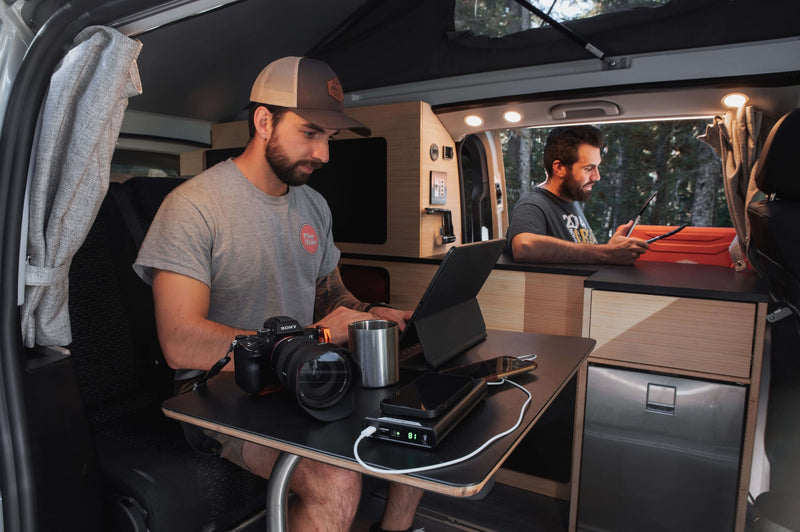 a person cooks in a pop-top camper van's kitchen. Cozy mobile living with a bed.|Dark blue RV rental van on a gravel road — photo 7