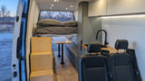 Explore this versatile RV rental interior featuring a cozy bed, compact kitchen, and dining area. Perfect for your next adventure!