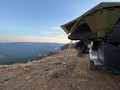 RV rental adventure: a rooftop tent on a trailer offers epic cliffside views over a valley at sunset.