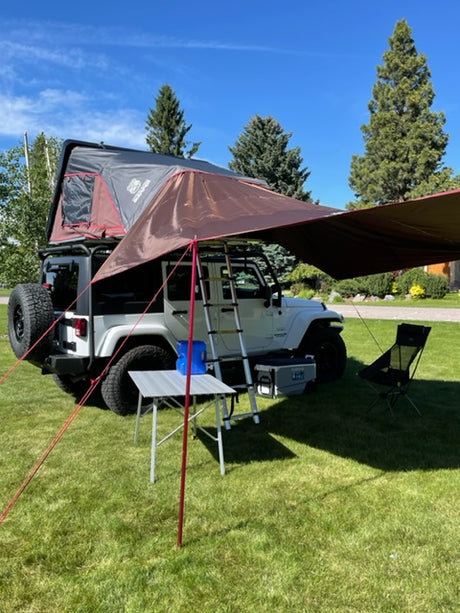 An RV rental equipped white Jeep with rooftop tent and awning on grass, ready for camping. Outdoor travel setup.