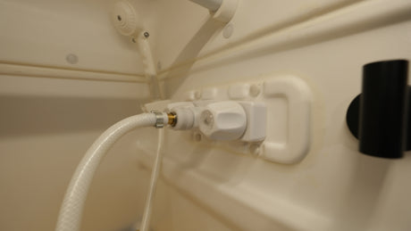 Close-up of an RV rental shower: The beige interior features water controls, a flexible hose, and a wall-mounted showerhead.